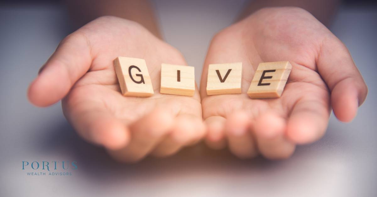 Two hands open palms facing upward holding Scrabble tiles that spell the word "GIVE".