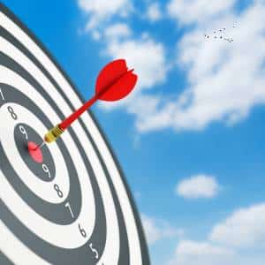 Dartboard with a dart in the bullseye. Cloudy blue sky in background.