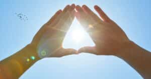 Image of a person holding their hands up in the sky and making a triangle shape in the negative space between their connected hands.