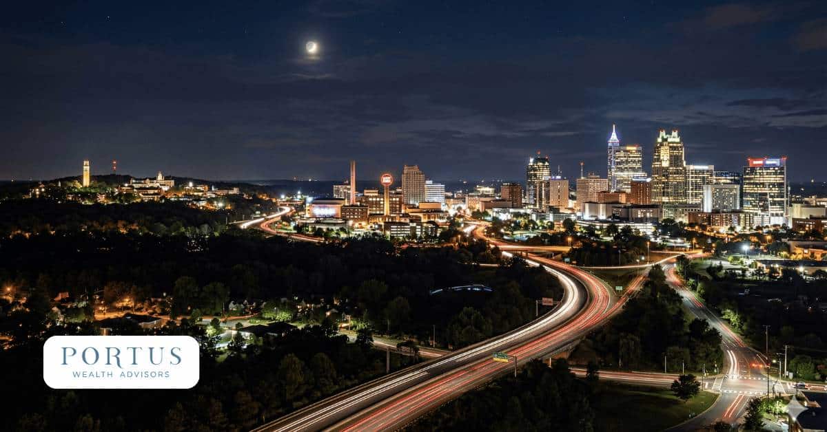 Raleigh, NC, Triangle, NC at night showing cars zipping along the highway around the city. Portus Wealth Advisors logo in the bottom left corner.