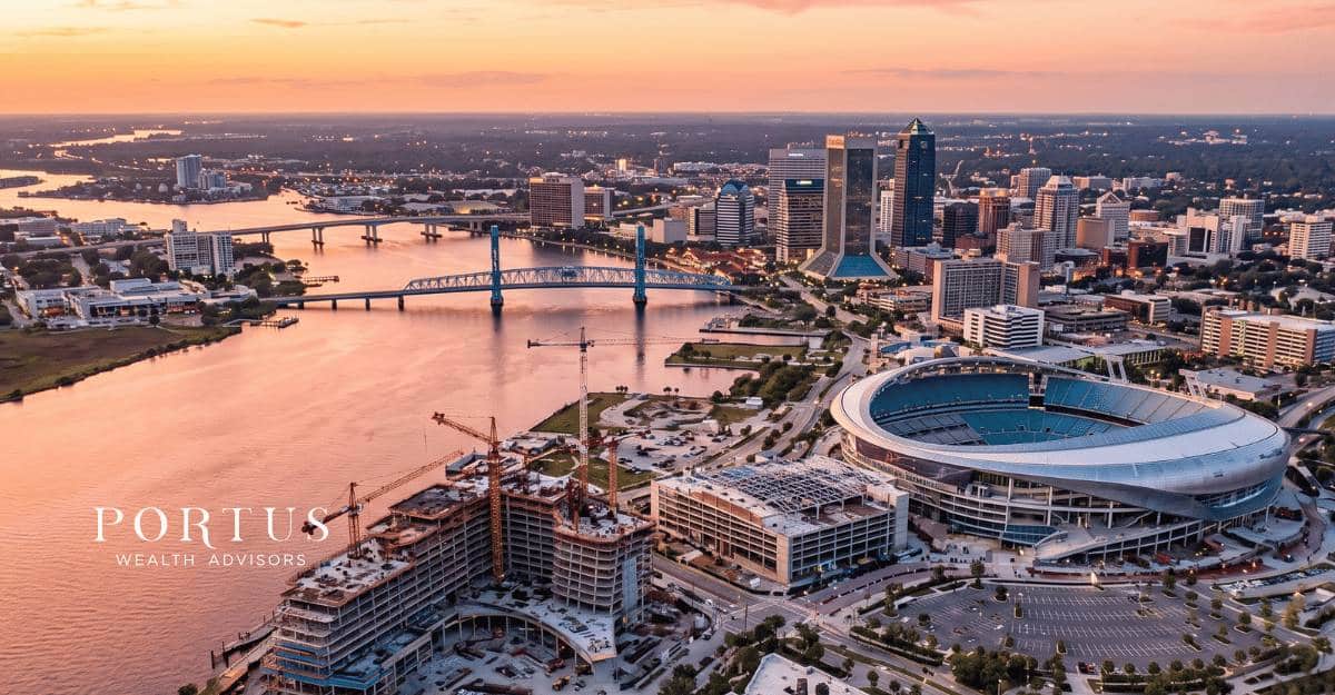 An aerial shot of the St. Johns River winding through downtown Jacksonville, FL at golden hour or twilight. Portus Wealth Advisors logo in the bottom left corner.