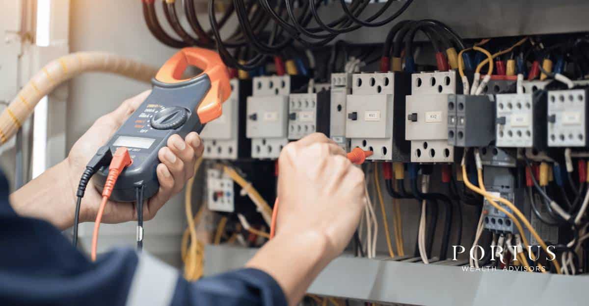 Open fuse box with the hands of an electrician testing the connection for the "selling a Triangle NC trades business" blog post. Portus Wealth Advisors logo in the bottom right corner.