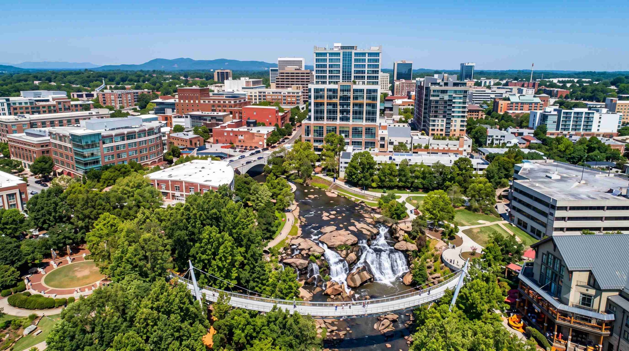 An aerial shot of downtown Greenville, SC with the Reedy River Falls visible. Portus Wealth Advisors logo in the bottom left corner.