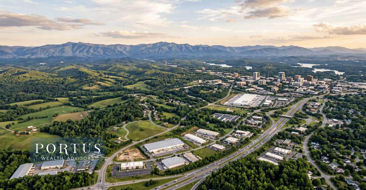 A wide cinematic aerial showing the Upstate's rolling piedmont landscape with the Blue Ridge visible in the background and a hint of industrial or commercial development in Greenville, SC. Portus Wealth Advisors logo on the bottom left corner.