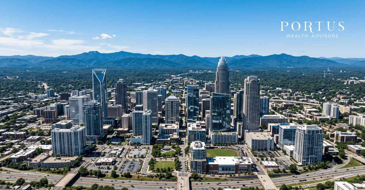 A cinematic wide-angle aerial of the Charlotte, NC skyline with the Blue Ridge visible in the distant background on a clear day for the "Selling Your Business in NC" blog post.. Portus Wealth Advisors logo in the top right corner.